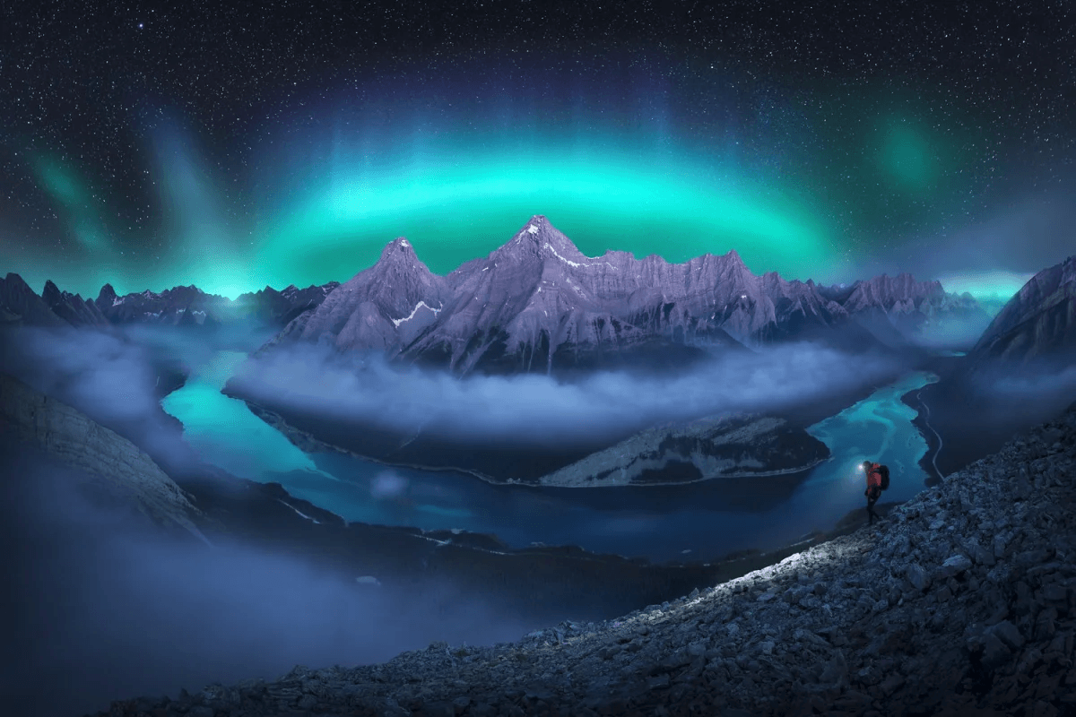A nighttime aurora mountain and river landscape with a hiker by one of the best nature photographers Cath Simard