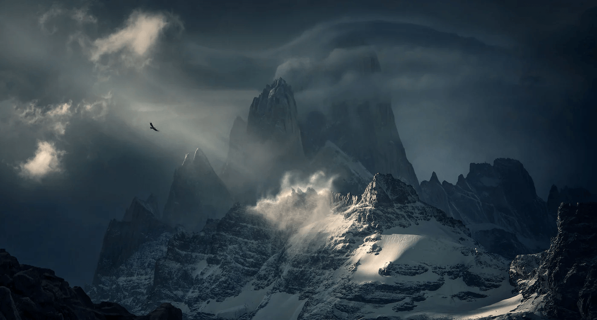 Rugged snowy mountains with a beam of sunlight and bird flying by one of the best nature photographers Max Rive