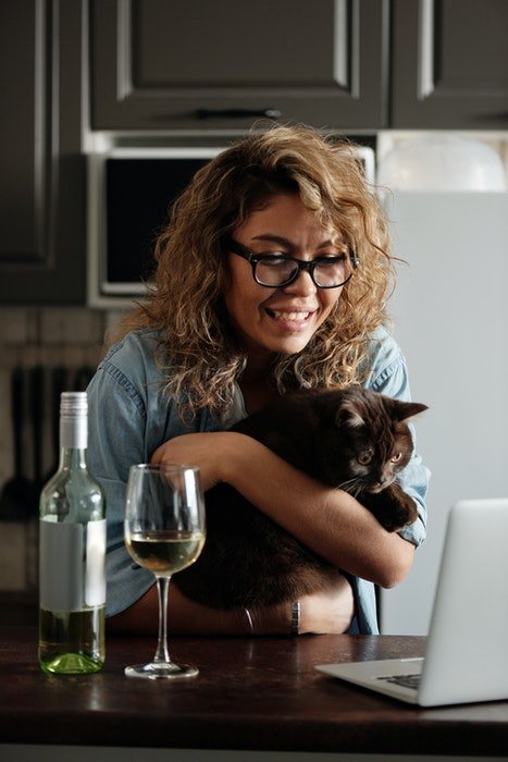 Cute portrait of a curly haired girl holding her cat in front of her laptop