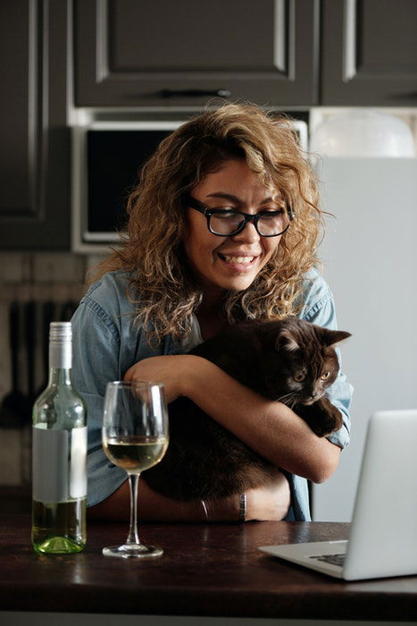 Cute portrait of a curly haired girl holding her cat in front of her laptop as an example of family photos with pets