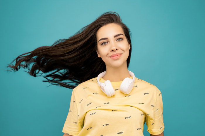 Portrait photo of a woman wearing a ellow tshirt in front of a blue backdrop 