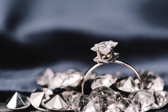 A diamond ring on dark background with other diamonds around it. 