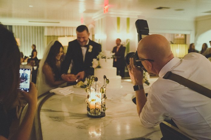 A wedding photographer taking a portrait of the happy couple cutting a cake
