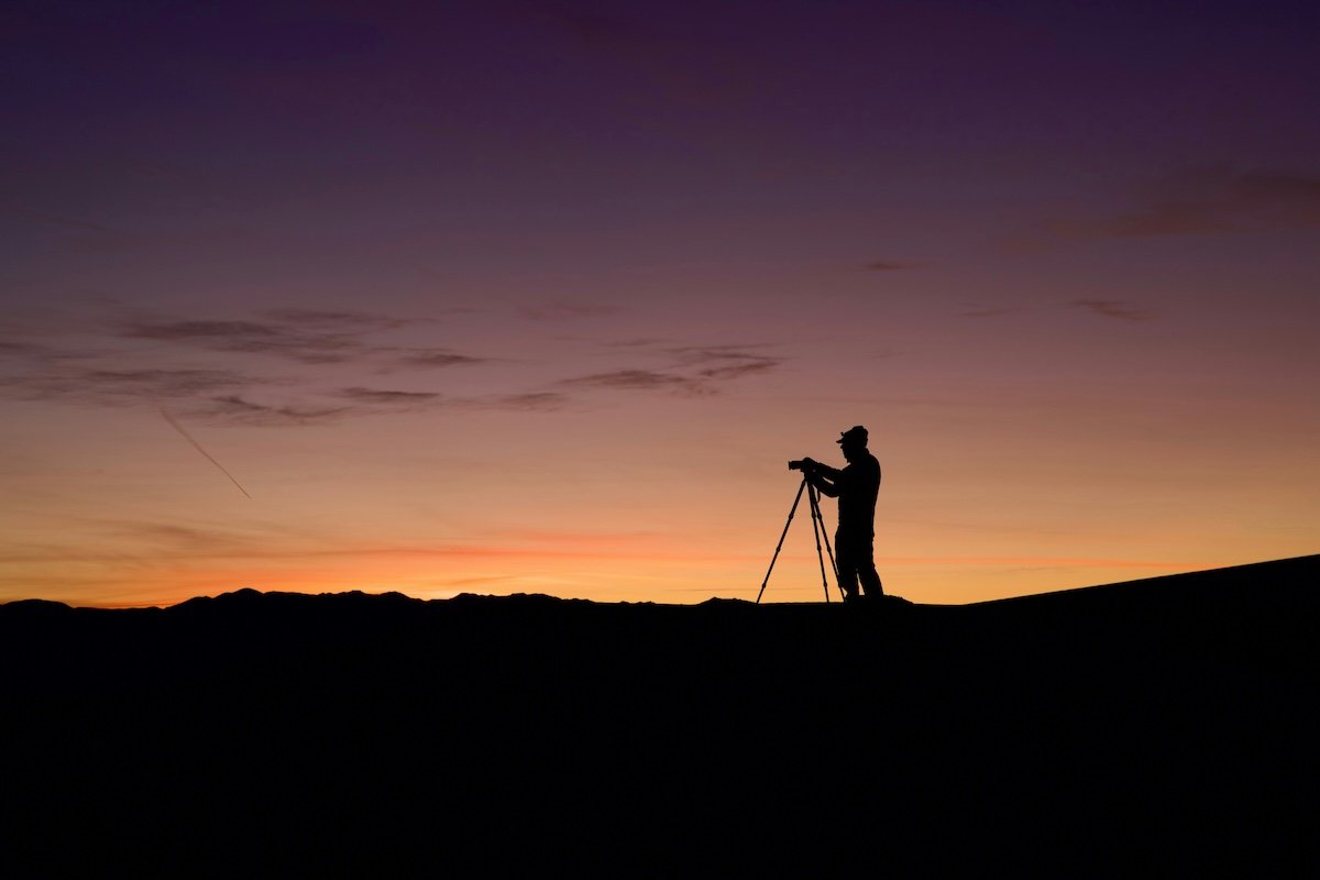 Silhouette of a photographer and tripod on a ridge at sunrise for a photography challenge