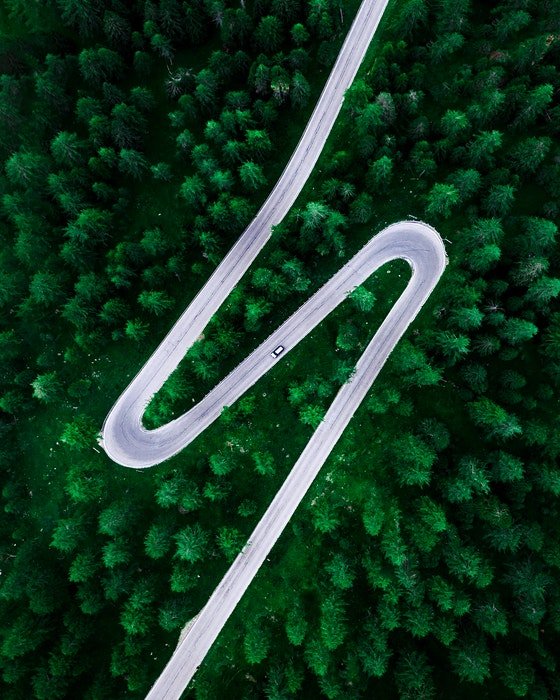 Photo of a curvy road in the middle of a forest from bird eye