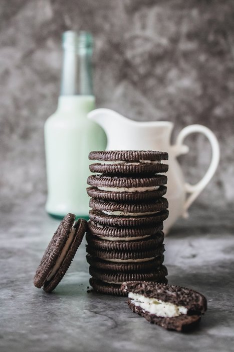 A stack of chocolate cookies in front of a jug of milk