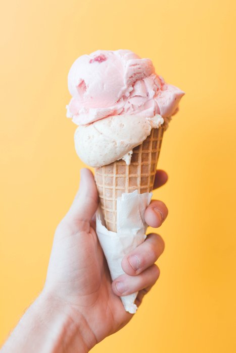 Hand holding a strawberry ice cream in front of yellow background