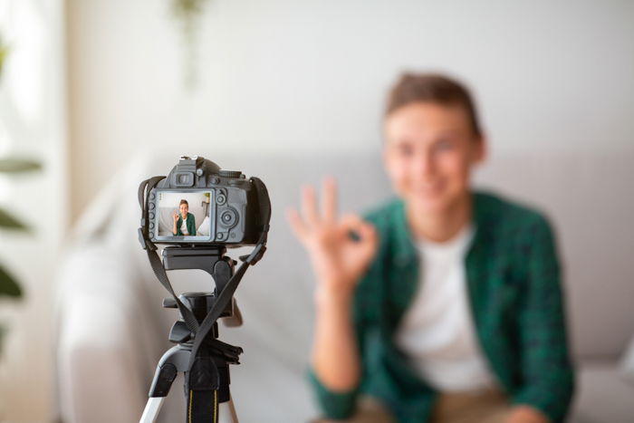 Selective focus on camera shooting teen guy showing okay gesture.