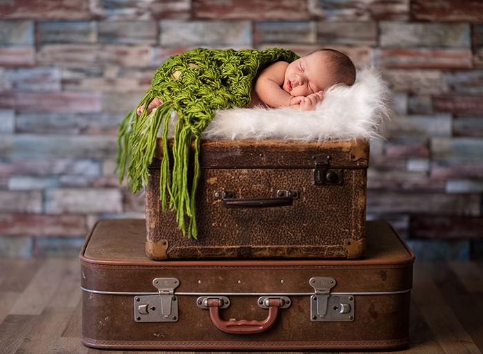 Little newborn baby sleeping on rustic suitcases