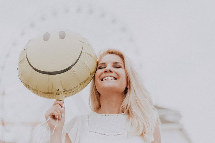 Woman smiling and holding a smiley face baloon