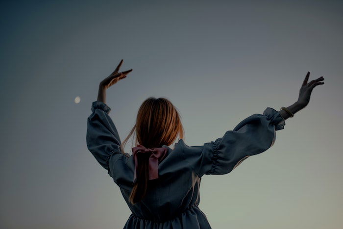 Woman raising her hands over her head at dusk