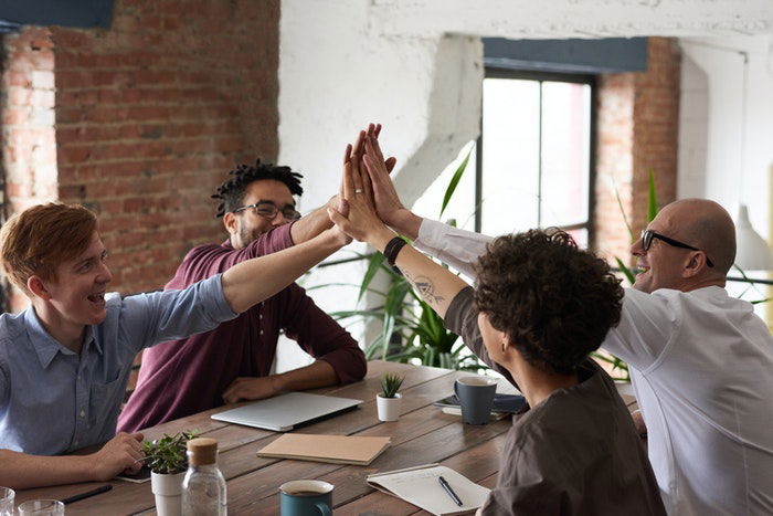 Four coworkers giving each other high-fives across a table