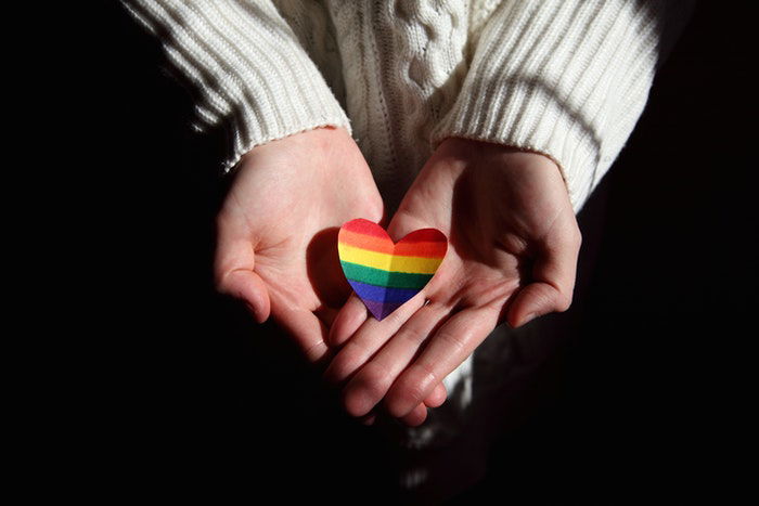 A close up of cupped hands holding a rainbow colored paper heart