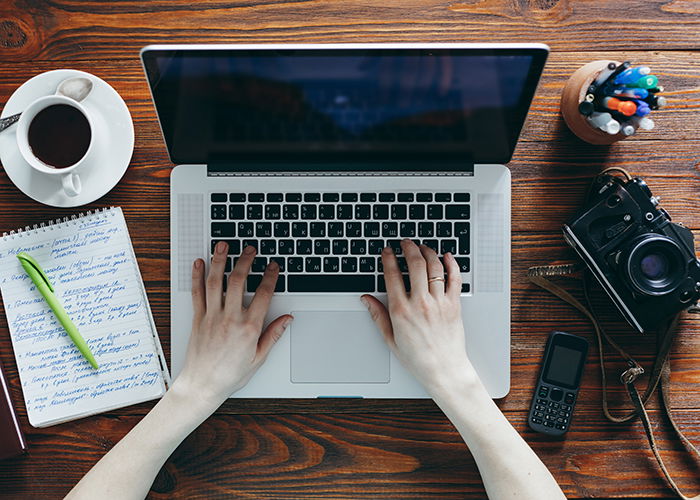 An image of a desktop with coffee, notes, a laptop and a camera.