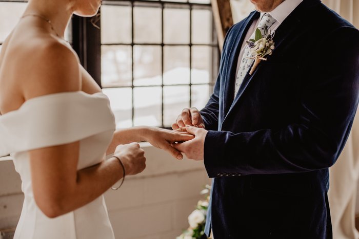 A groom placing a wedding ring on a bride's hand as an idea for wedding photography posing