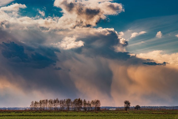 A storm cloud with rain coming down from it over a landscape with som sun and blue sky