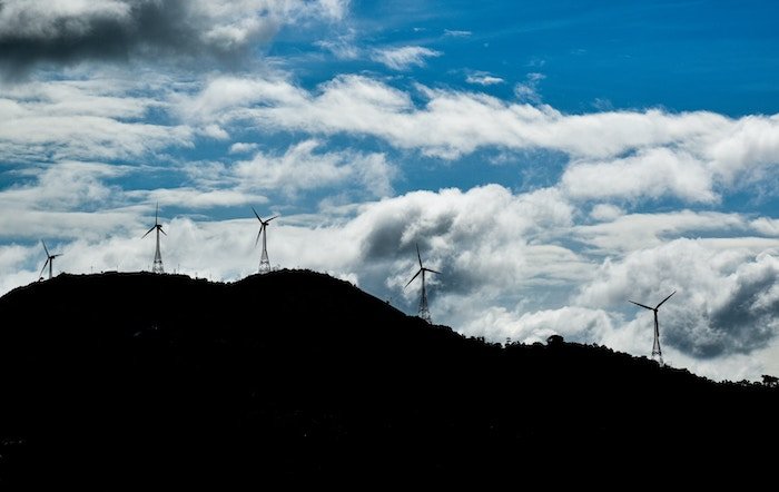 Silhouette of wind turbines on a hill with a backdrop of white clouds