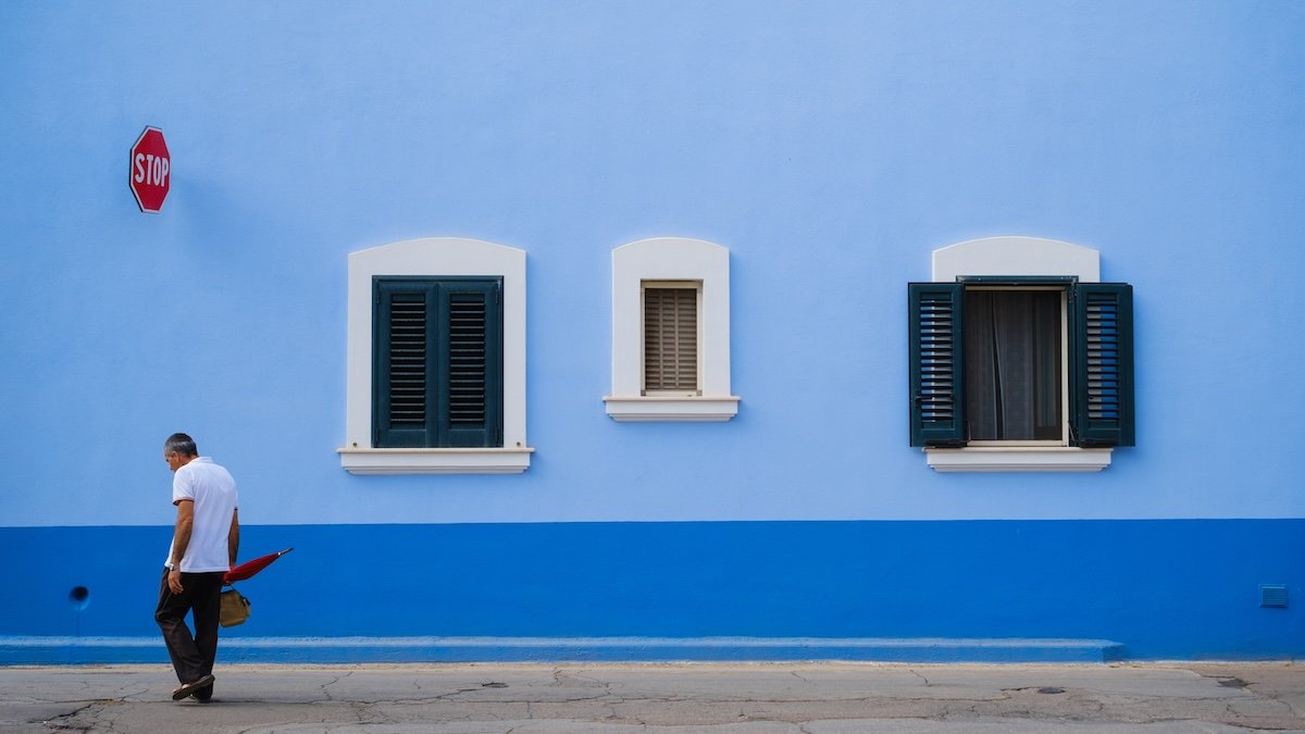 A man walking in front of a blue wall with windows to illustrate exposure in photography