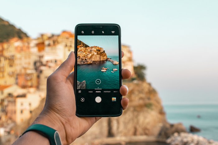 photo of someone taking a photo of a beautiful coastline with a smartphone