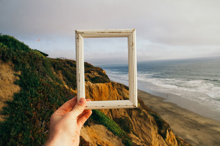 A person holding a picture frame up to a landscape