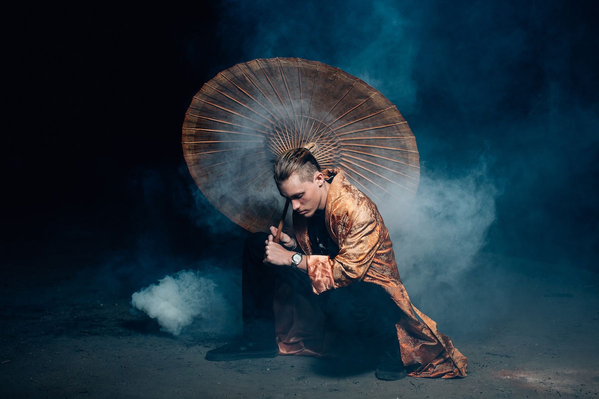 Portrait of a man in traditional Japanese clothes crouching and holding an umbrella with smoke around him