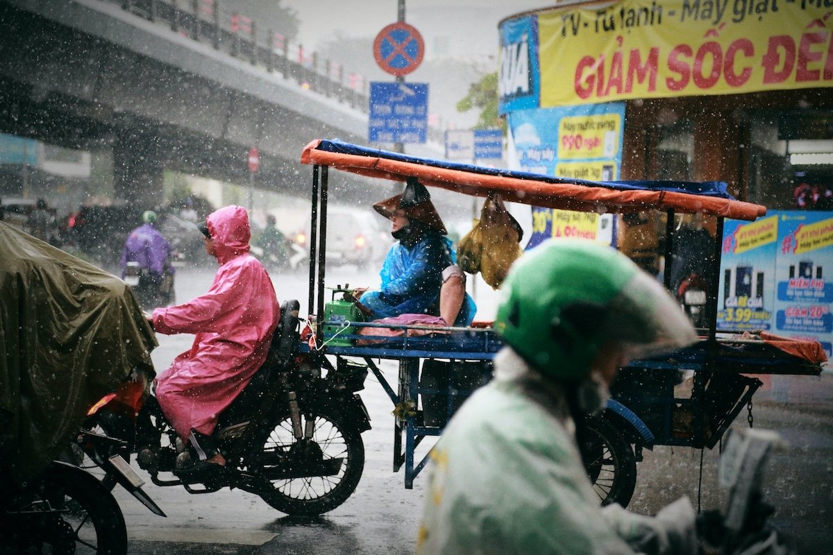 A frozen rainy street scene in Vietnam with motorcyclists and carts shot with a fast shutter speed