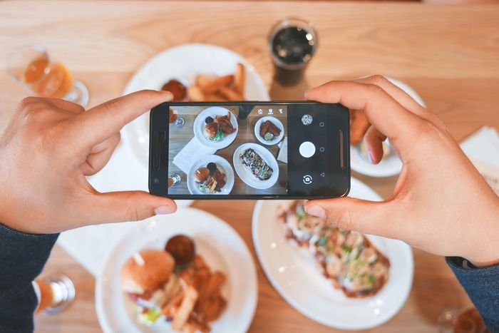photo of hands holding a smartphone to take a photo of plates of food