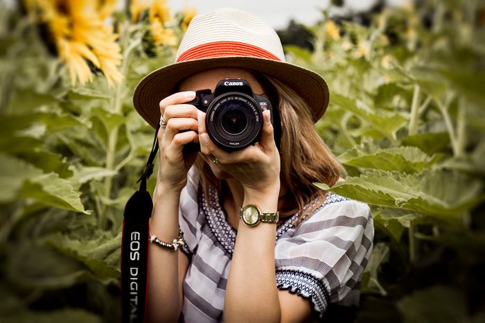 A girl in a sunflower field taking a photo with a DSLR camera