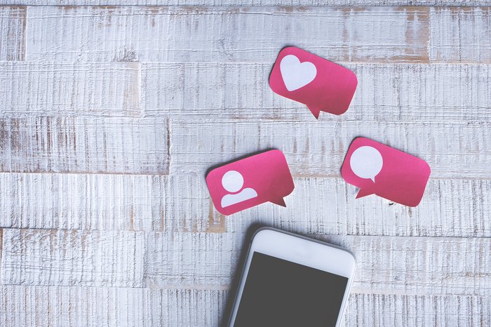 A smartphone with pink paper social share and likes icons above it