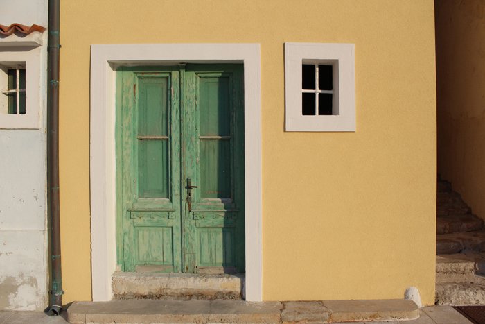 an image of a green door within a yellow building with small window to its right