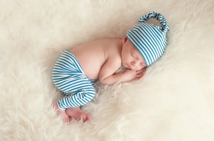 Newborn baby in striped trousers and hat on a furry blanket