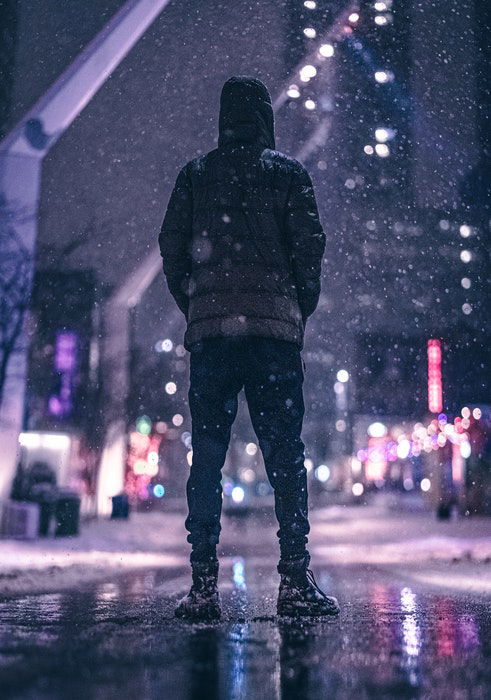 A man in winter clothes standing on a city street while its snowing