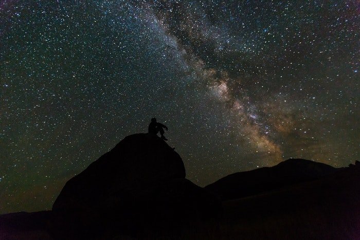 Stunning astrophotography shot of the silhouette of a man on a rock in front of a star filled sky
