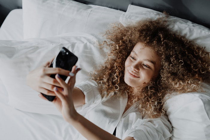 A girl taking a selfie laying down in bed taking a selfie while smiling