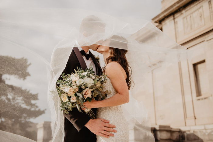 a bride and groom kiss as her veil blows in the wind