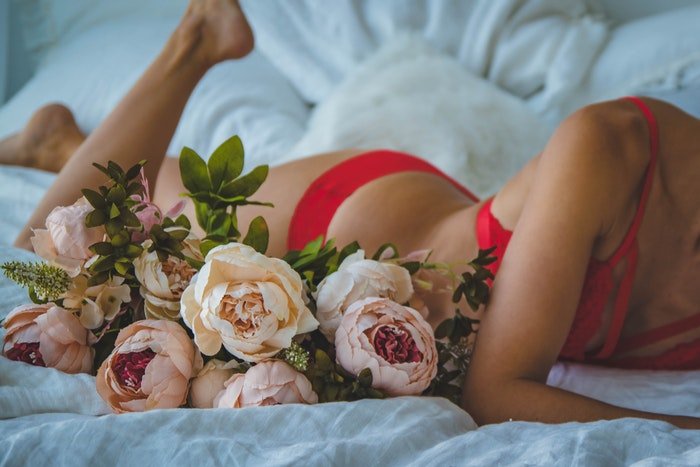 A close up of a girl in red lingerie posing on a bed for a bridal boudoir photoshoot