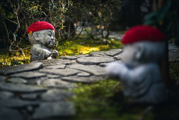 Two stone Buddha sculptures with red knitted hats