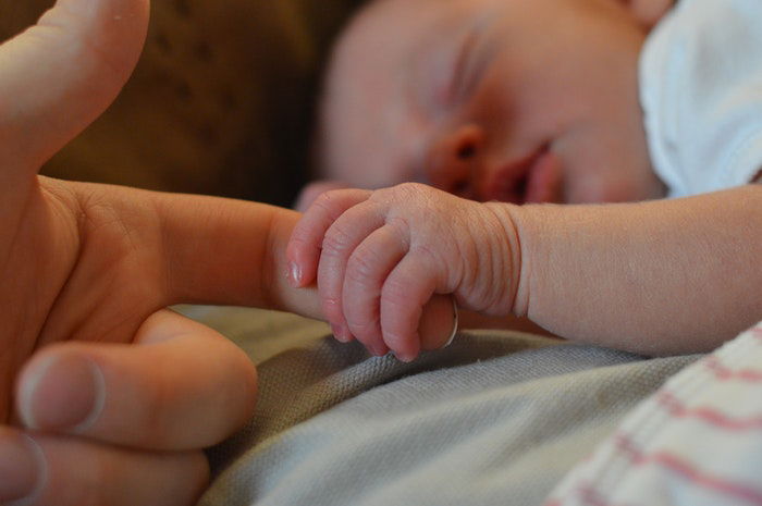 A newborn baby holding their mothers finger