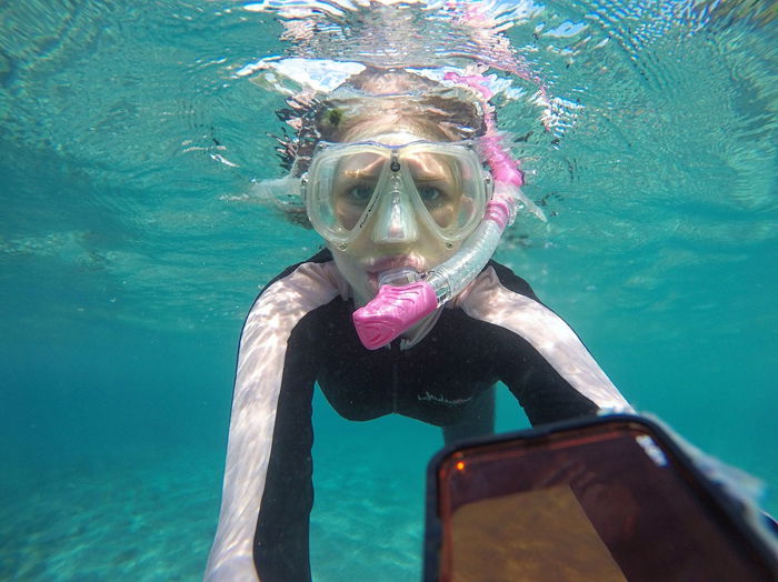 A snorkeling girl taking a selfie underwater