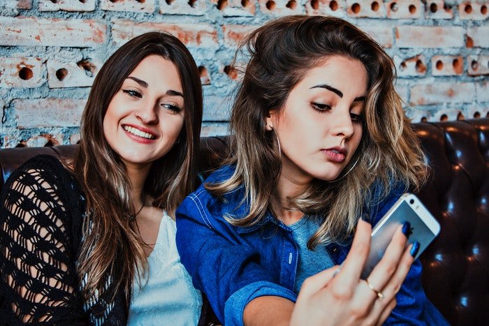 Two teen girls sitting on a couch taking a selfie photo