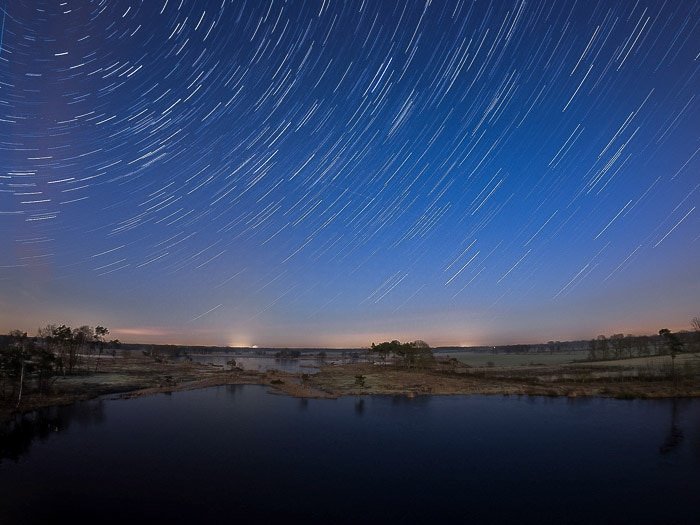 Nocturnal landscape over water and star trails above for creative motion blur