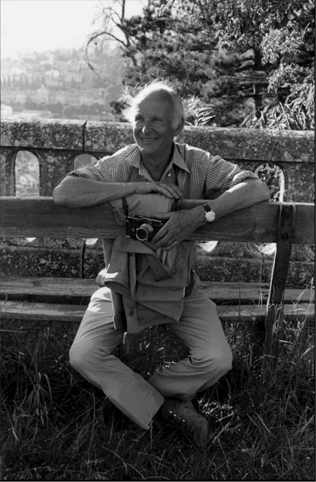 a black and white image of henri cartier-bresson sitting on a bench in forcalquier france in 1972