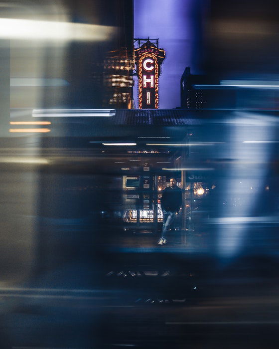 Blurry impressionist style street portrait of a man leaning on a pole at a train station