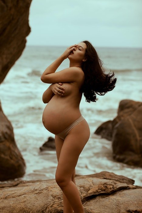 Beautiful maternity boudoir photo of a pregnant woman posing naked on the beach