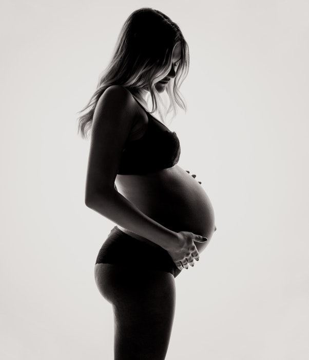 Black-and-white side-view photo of a woman posing in lingerie for pregnant boudoir photography