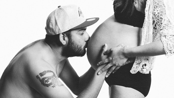 Black-and-white maternity photo of a man kissing his wife's belly for pregnant boudoir photography