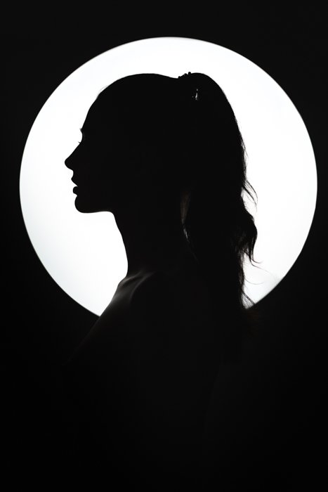 Fine art silhouette of a young woman against the round light source. 