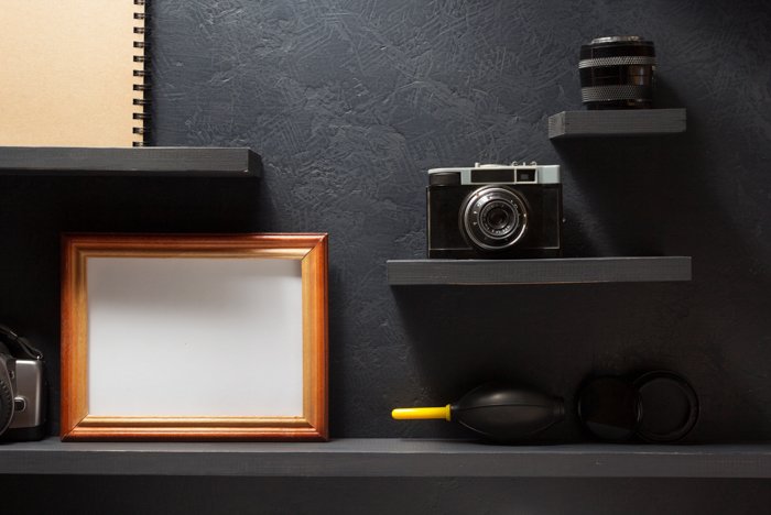 An old camera, a lens, and a picture frame on a wooden shelf