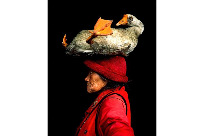 An old lady in red clothes and a hat, and a goose on top of the hat.