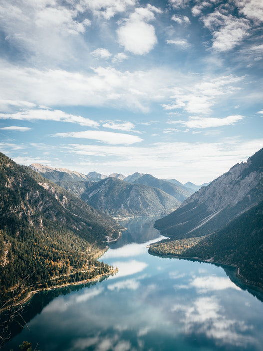 a landscape shot of a river cutting through a mountain range with clouds and sky above